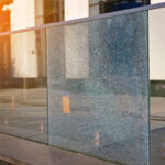 Damaged tempered glass fence. Broken glass fence with banisters. Broken guard rail on office terrace. Steel railing with damaged panel, cracks on broken tempered glass. Fencing repair